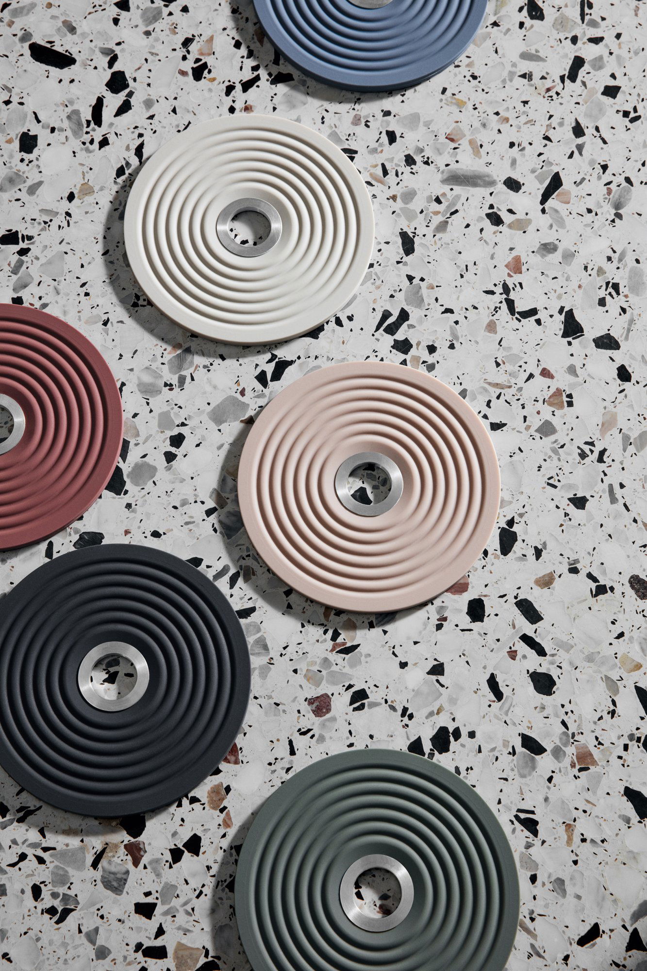 Bunte runde Untersetzer mit strukturierten Designs, die auf einer Terrazzo-Oberfläche angeordnet sind.