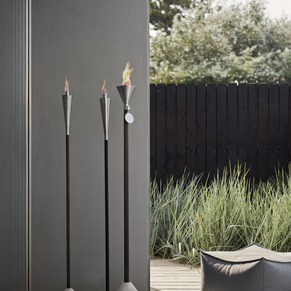 Elegante Gartenfackeln mit Flammen neben einem modernen Sitzbereich und üppigem Grün.