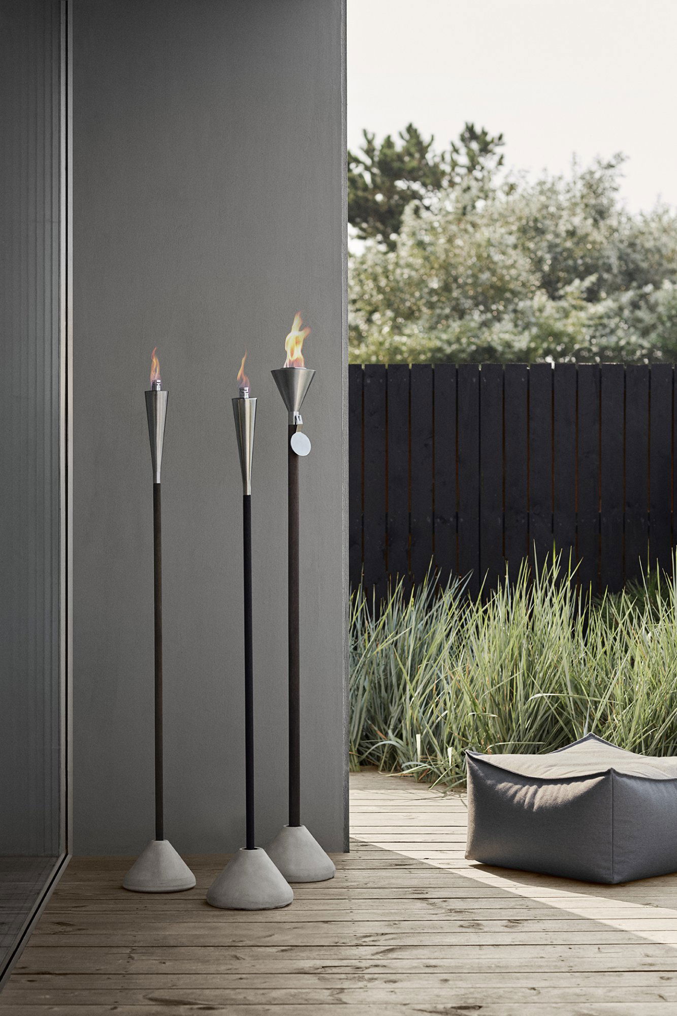 Elegante Gartenfackeln mit Flammen neben einem modernen Sitzbereich und üppigem Grün.
