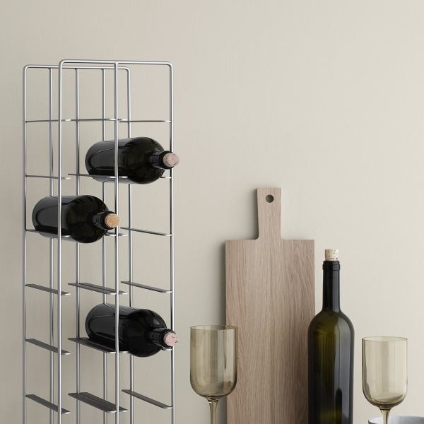 Modern wine rack with bottles, glasses, and a wooden cutting board on a neutral wall.