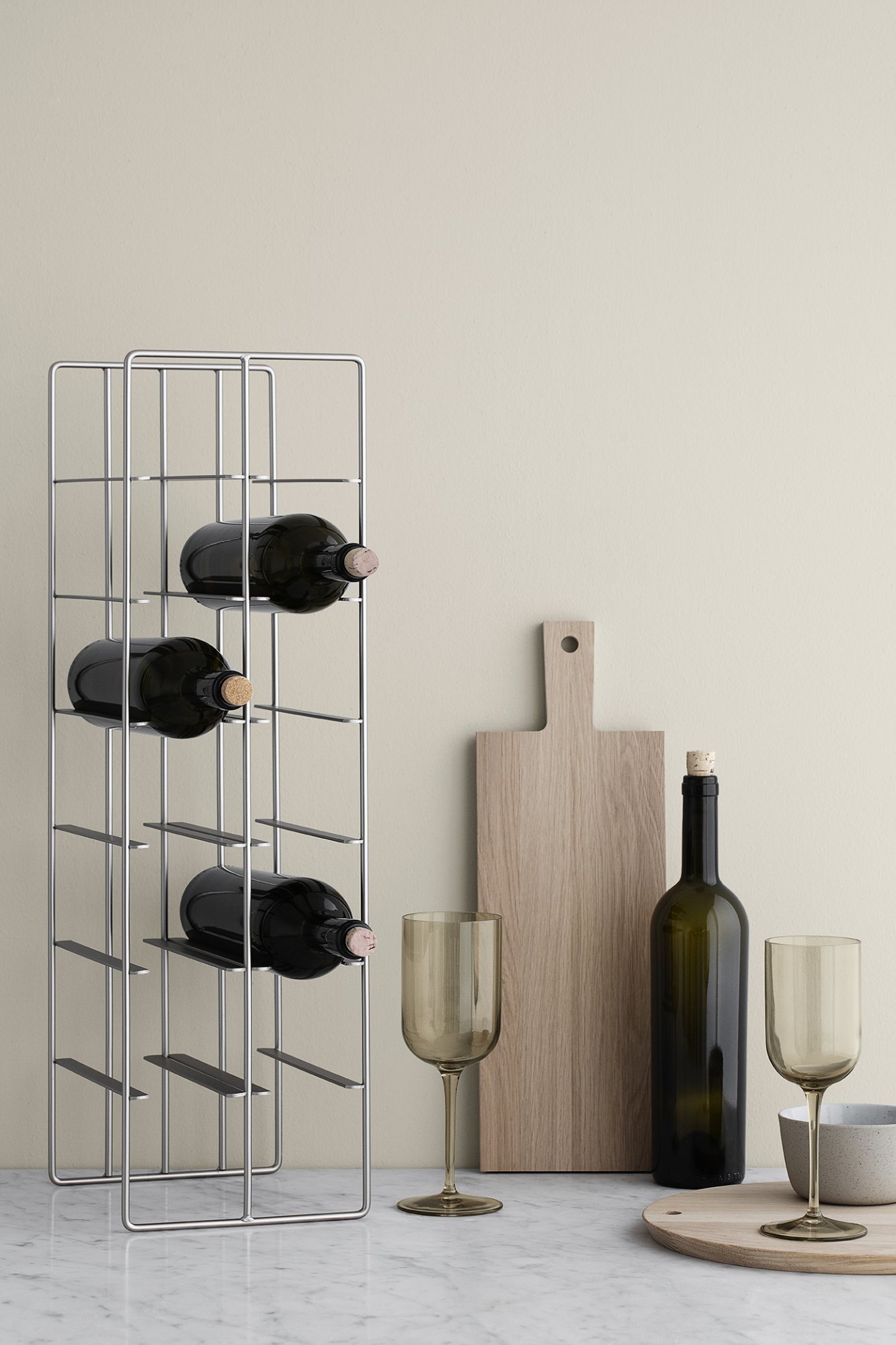 Modern wine rack with bottles, glasses, and a wooden cutting board on a neutral wall.
