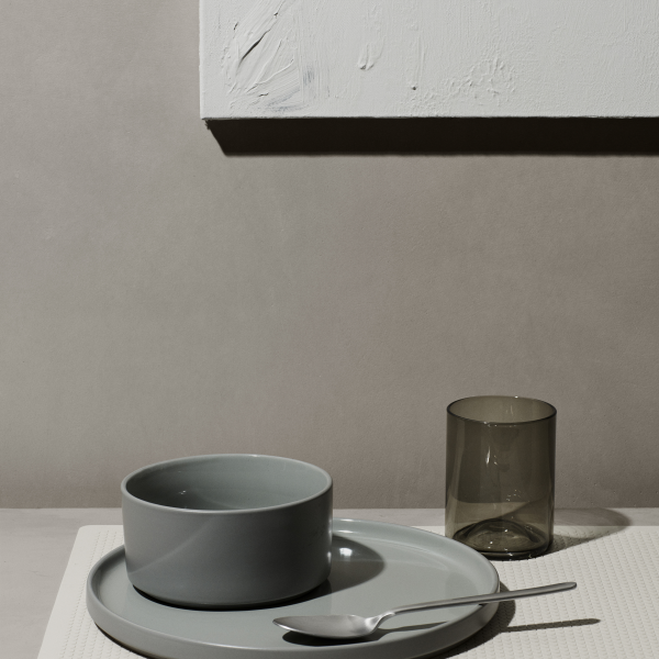 Elegant table setting with gray dishware and minimalist decor against a soft wall backdrop.