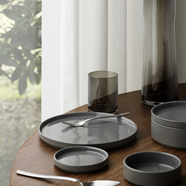 Elegant table setting with gray dishes, glasses, and cutlery on a wooden surface.