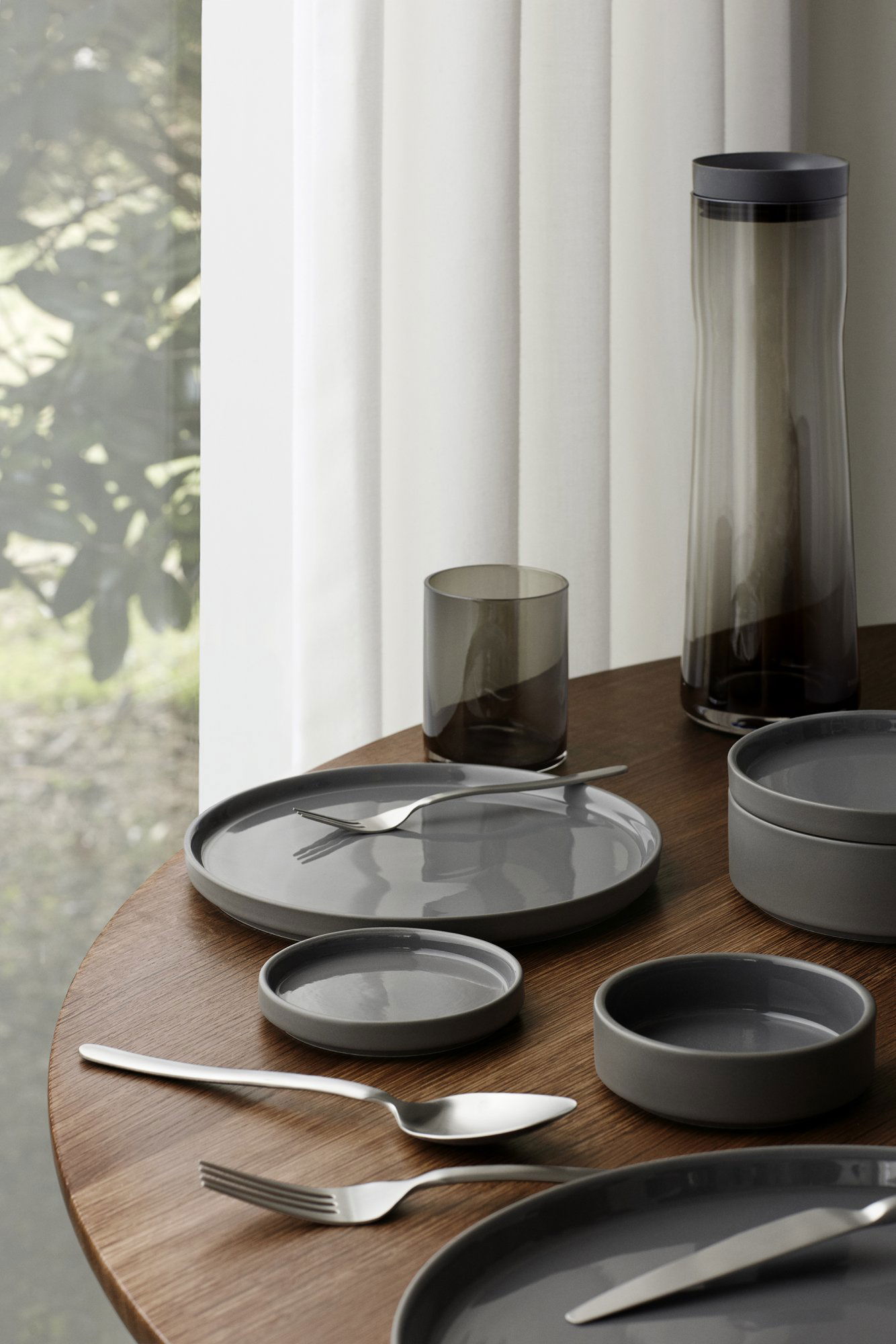 Elegant table setting with gray dishes, glasses, and cutlery on a wooden surface.