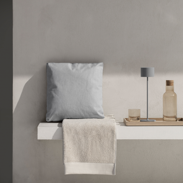 Modern gray pillow and simple decor on a minimalist shelf with a glass and a bottle.