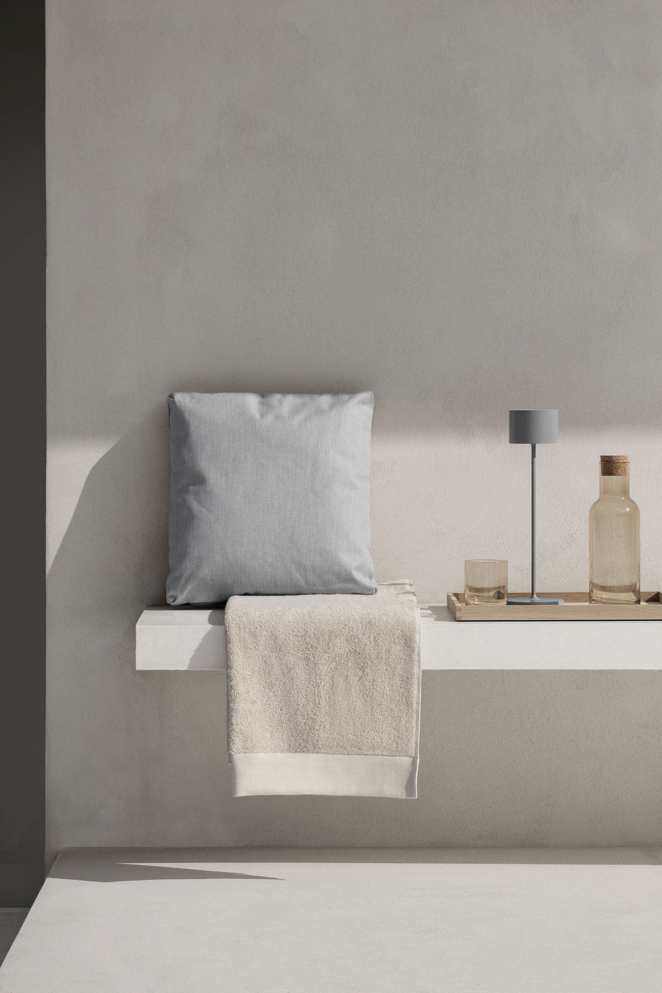 Modern gray pillow and simple decor on a minimalist shelf with a glass and a bottle.