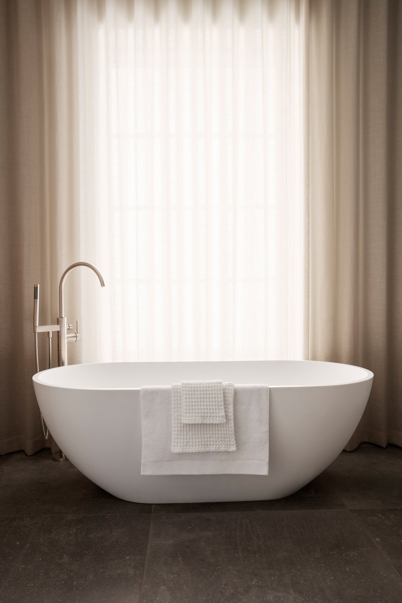Modern bathroom featuring a sleek freestanding tub with a white towel draped over it.