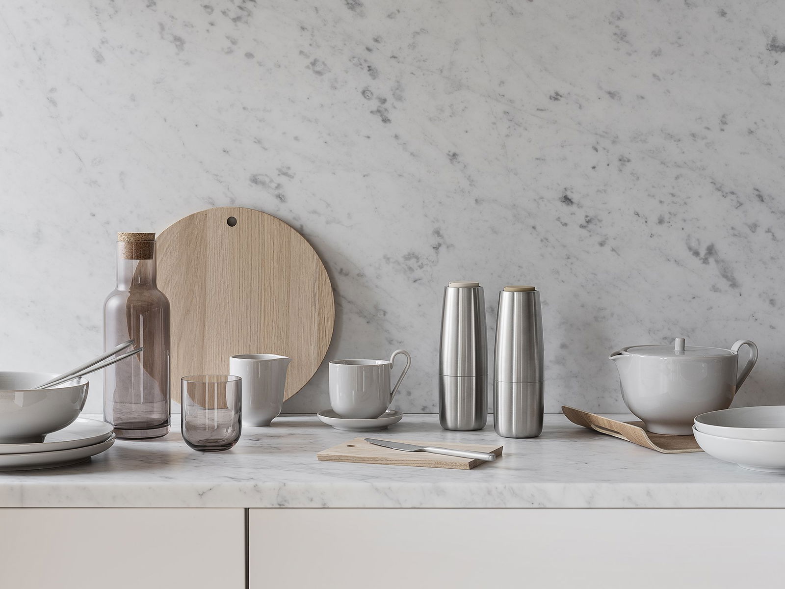 Modern kitchenware display with glass, stainless steel, and wooden elements on marble countertop.