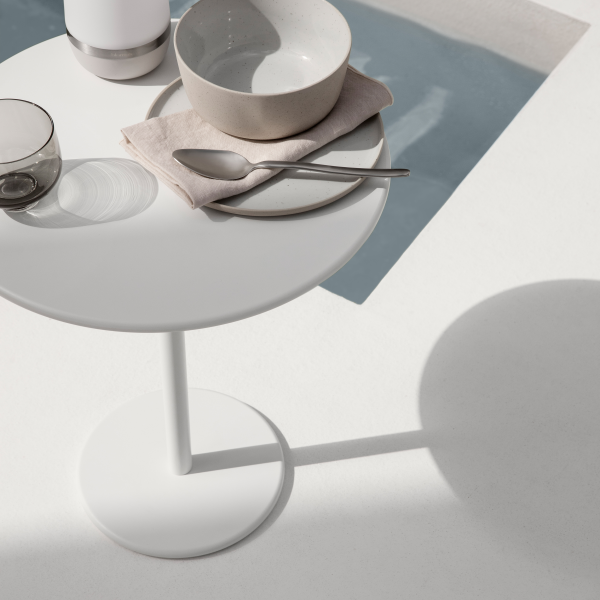 Minimalistisches Esssetup auf einem weißen Tisch mit Tellern und Gläsern neben einem Pool.