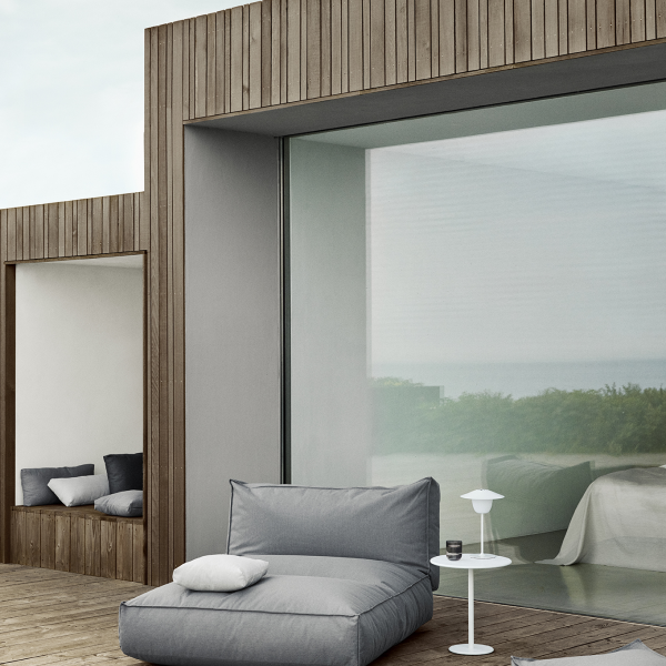 Modern outdoor space with cozy furniture and glass walls overlooking nature.