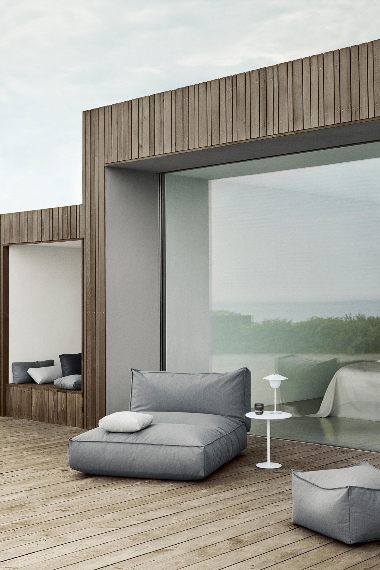 Modern outdoor space with cozy furniture and glass walls overlooking nature.