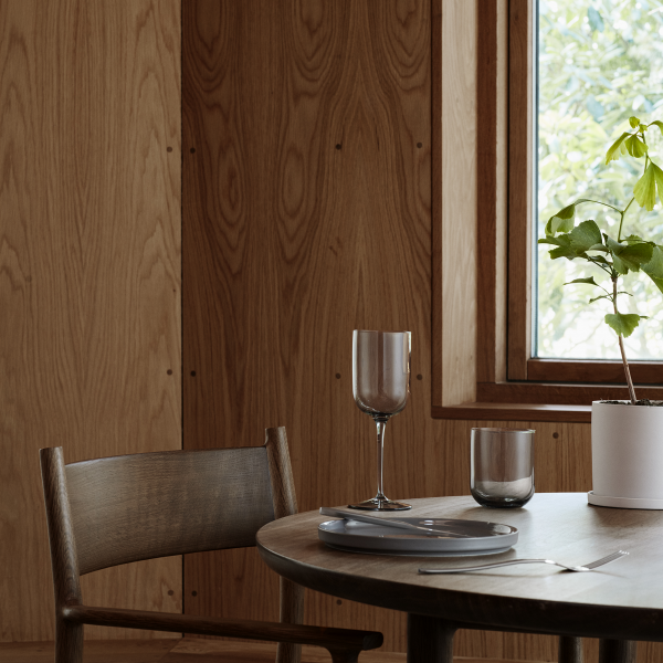 Modern dining setting with wooden walls, a table, glasses, and a potted plant by the window.