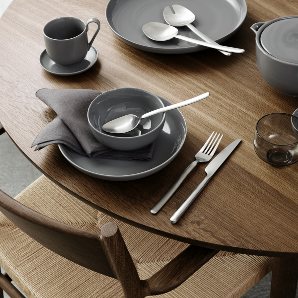 Elegantes graues Esszimmer-Set auf einem Holztisch mit Besteck und einer Serviette arrangiert.