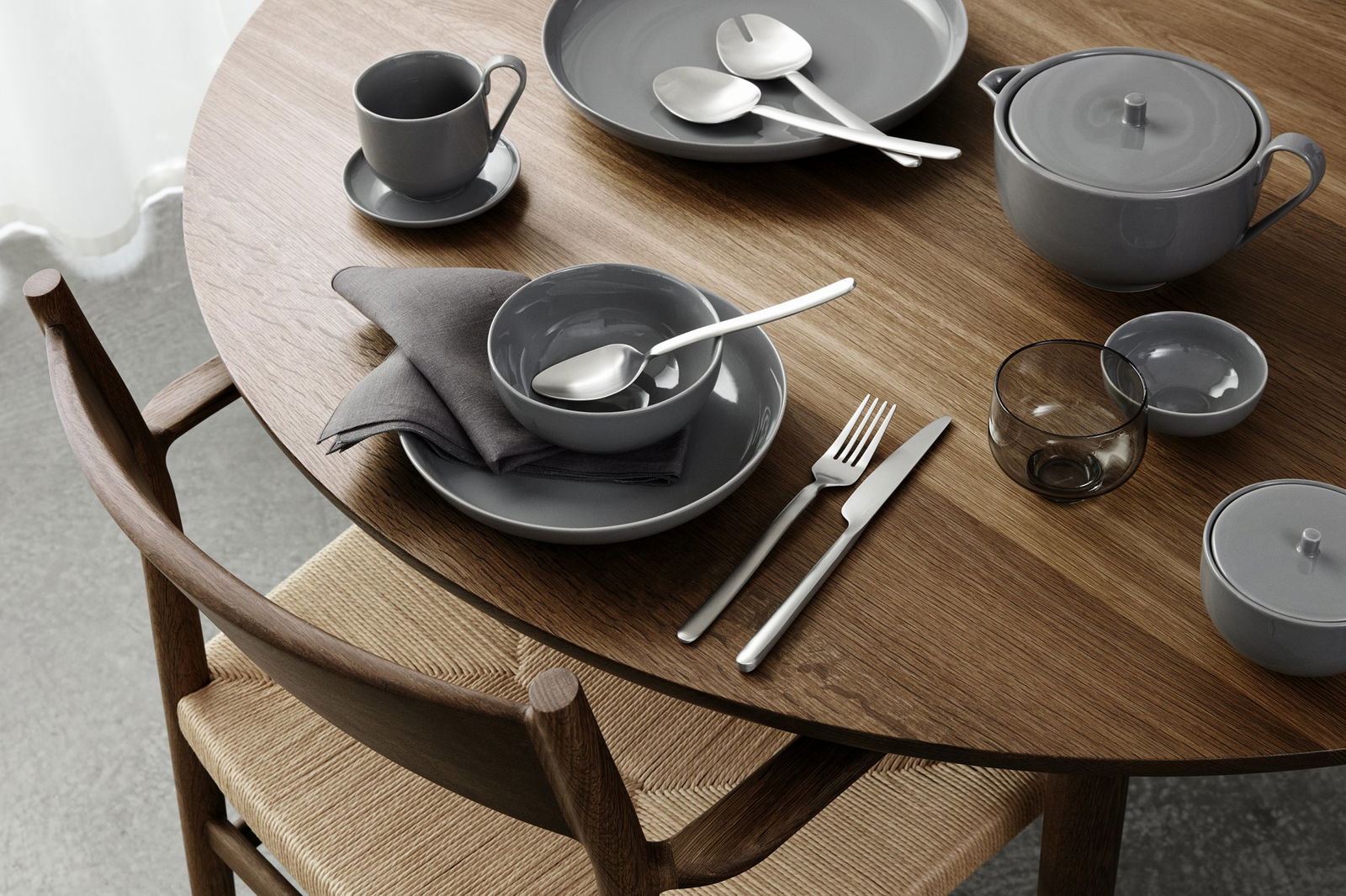 Elegantes graues Esszimmer-Set auf einem Holztisch mit Besteck und einer Serviette arrangiert.