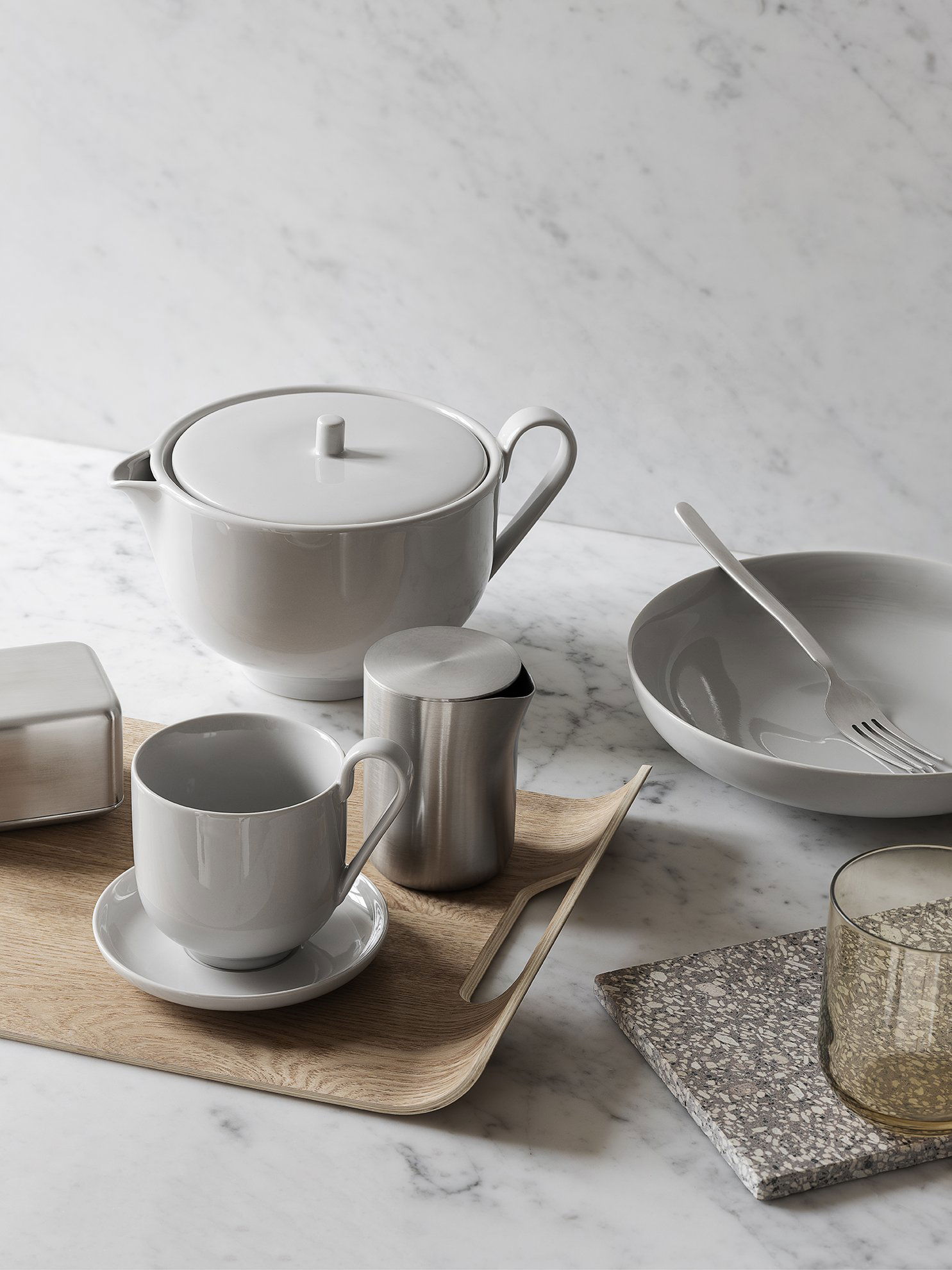 Elegant gray ceramic tea set with a wooden tray and minimalist dinnerware on a marble surface.
