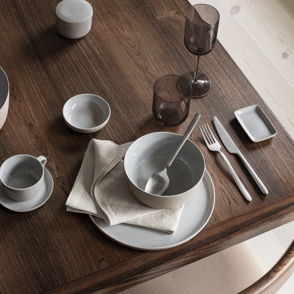 Modernes Esstischset mit elegantem Geschirr, Besteck und Glaswaren auf einer Holzoberfläche.