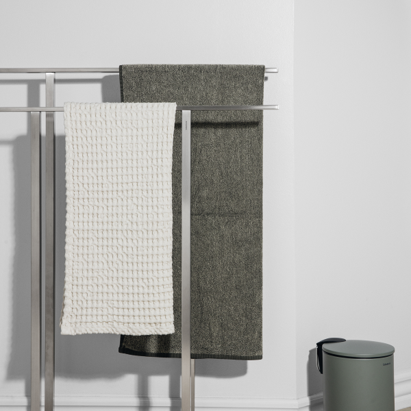 Stylish towels hanging on a sleek rack with a minimalistic trash bin in the background.