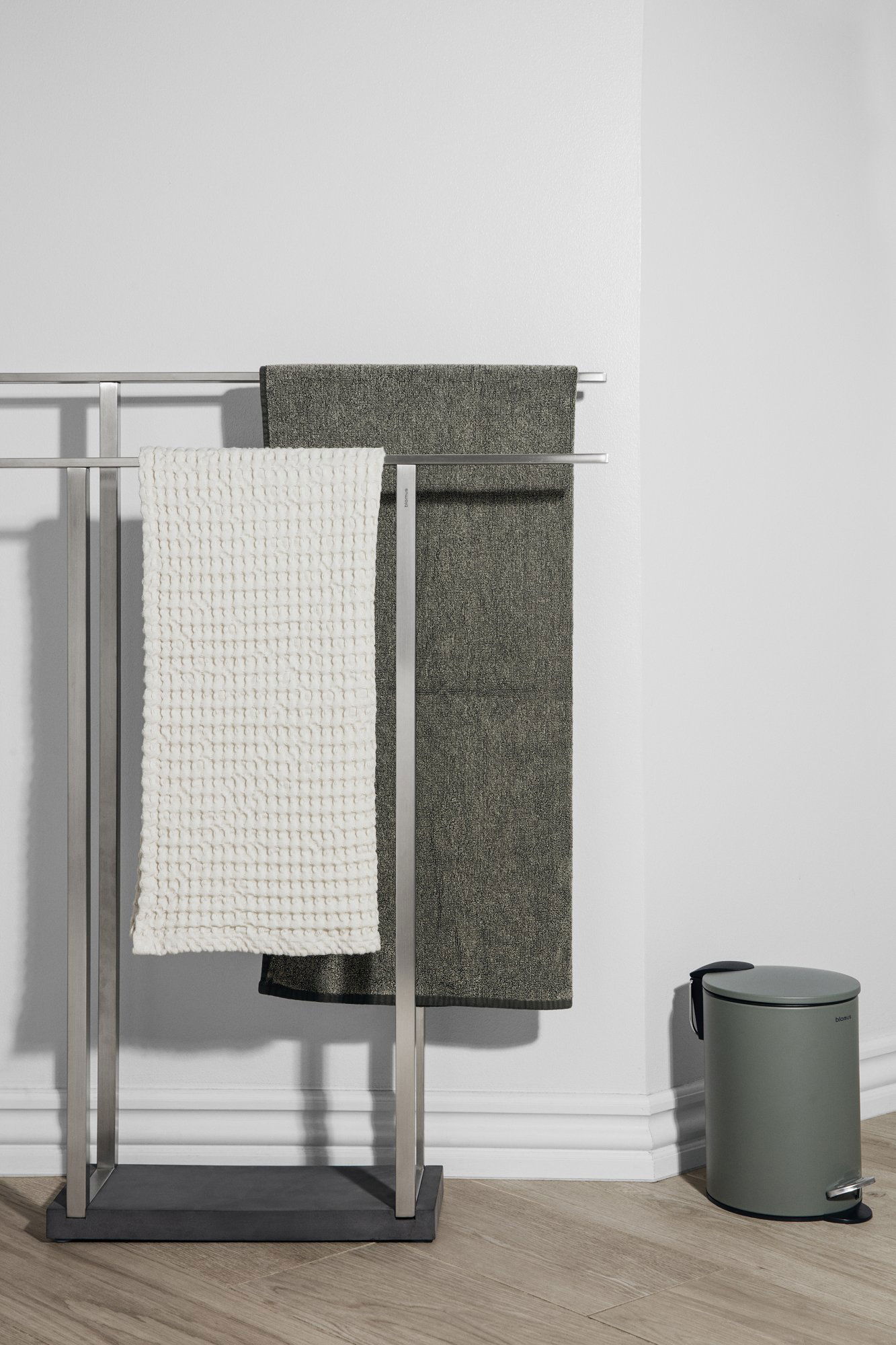Stylish towels hanging on a sleek rack with a minimalistic trash bin in the background.