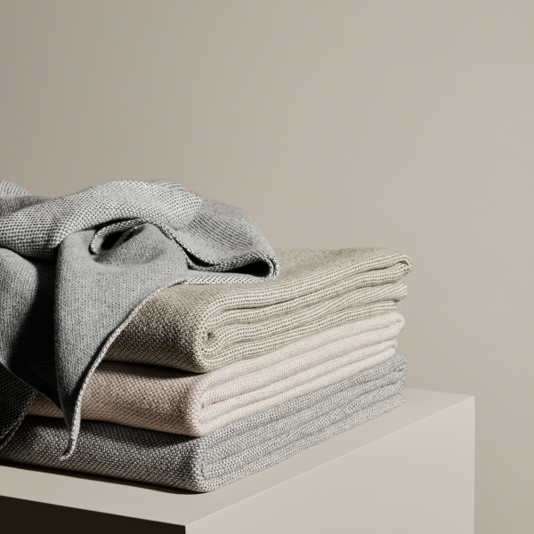 Weiche, gefaltete Handtücher in neutralen Farben auf einem minimalistischen Regal vor einem beigen Hintergrund.