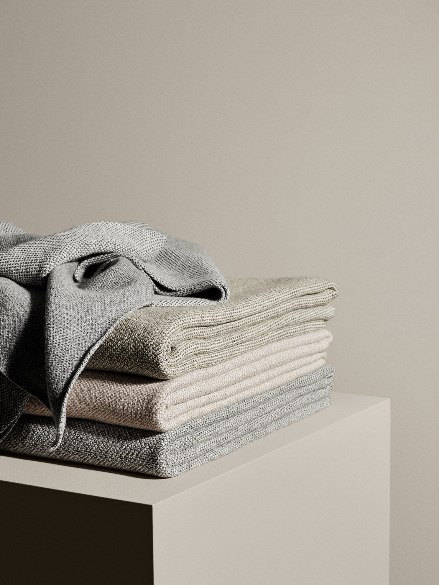 Weiche, gefaltete Handtücher in neutralen Farben auf einem minimalistischen Regal vor einem beigen Hintergrund.