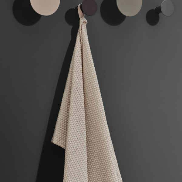 Beige strukturierte Handtuch hängt an einer minimalistischen grauen Wand mit runden Haken.