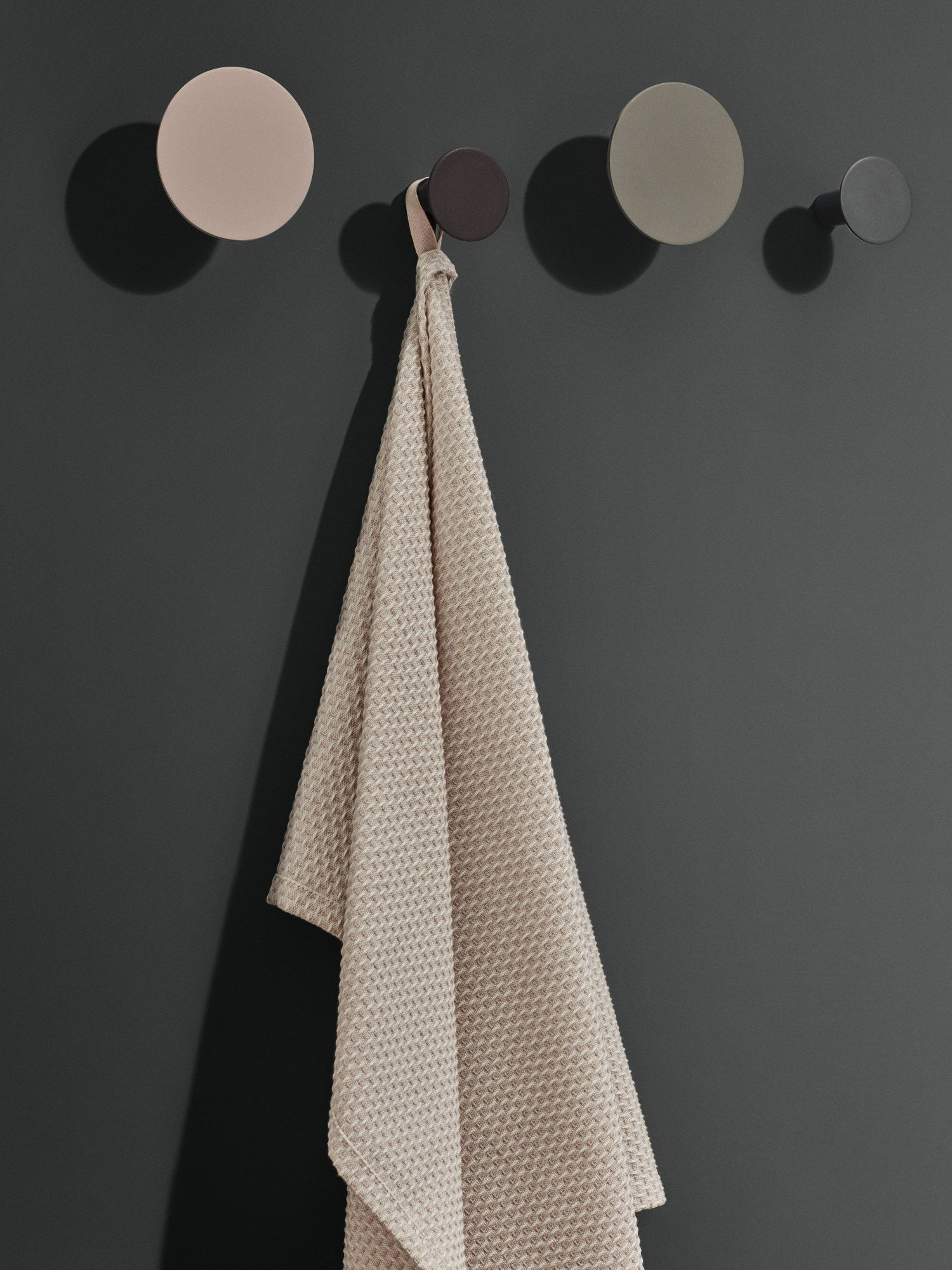 Beige strukturierte Handtuch hängt an einer minimalistischen grauen Wand mit runden Haken.