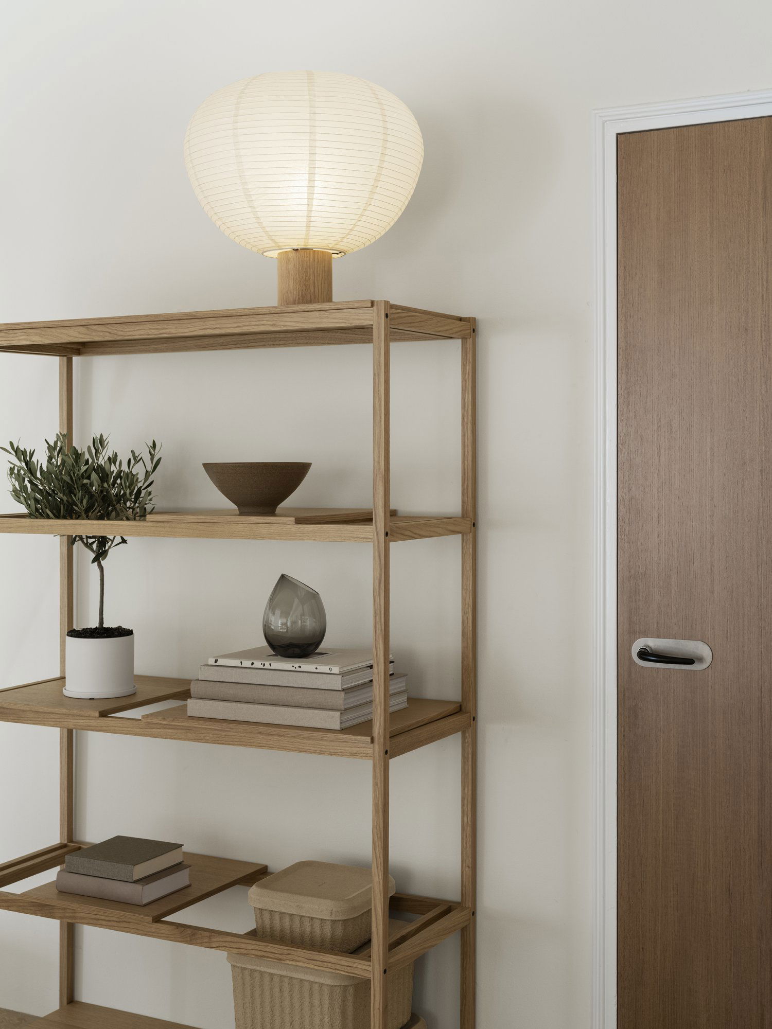 Gemütlicher Wohnraum mit einem Holzregal, dekorativen Gegenständen und einer warmen Lampe.