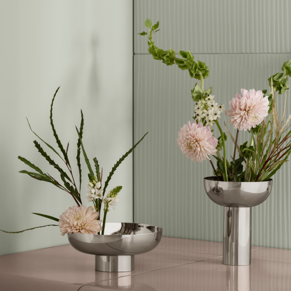 Elegante metallische Vasen mit gemischten Blumen auf einer sanft gefärbten Oberfläche und strukturiertem Hintergrund.