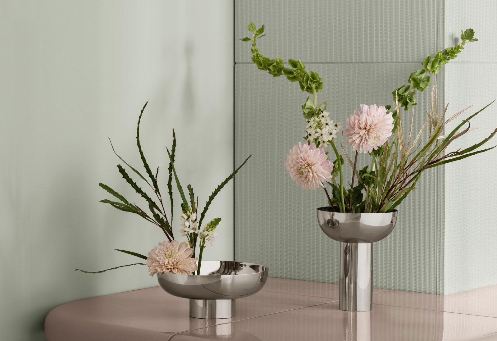 Elegante metallische Vasen mit gemischten Blumen auf einer sanft gefärbten Oberfläche und strukturiertem Hintergrund.