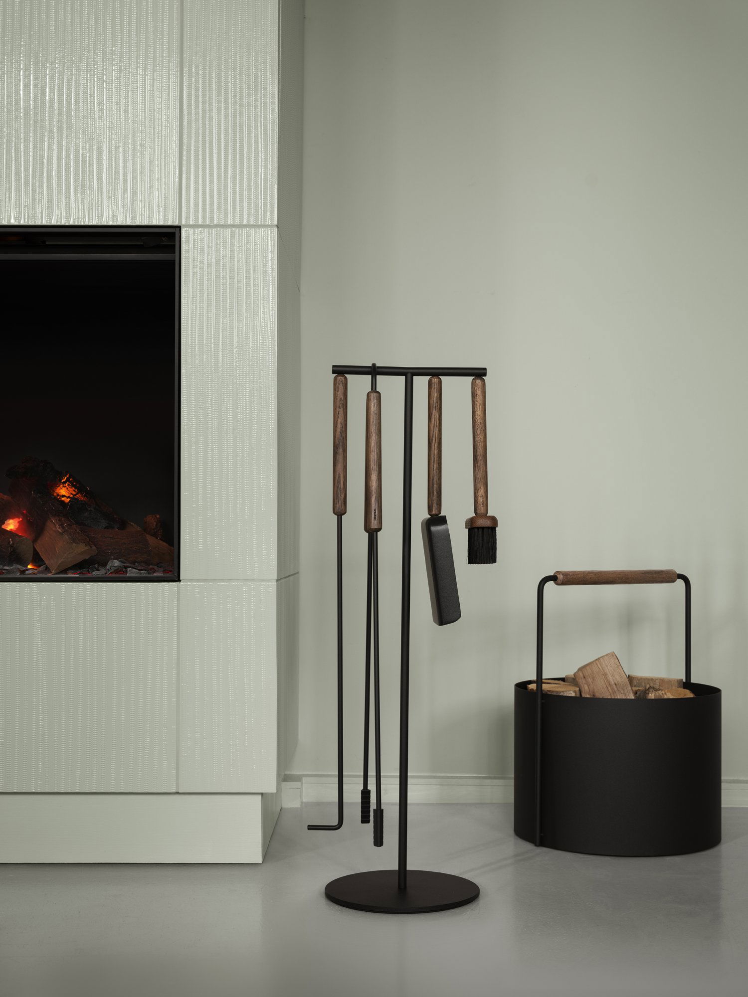Stylish fireplace tools with wooden handles beside a modern firewood holder.