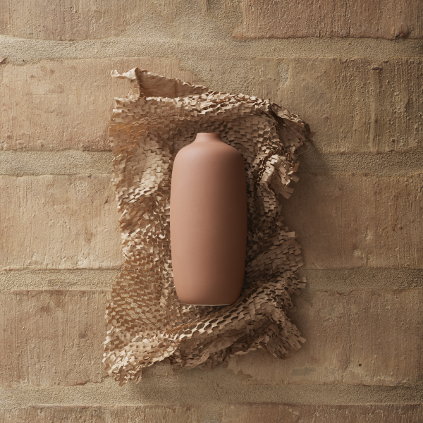 Minimalist brown vase on textured paper against a rustic brick wall background.
