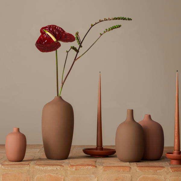Elegante Vasen mit einer auffälligen roten Blume auf einer rustikalen Ziegeloberfläche.