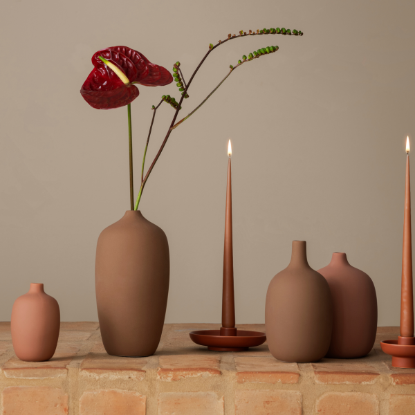 Stilvolle Keramikvasen mit lebhaften Blumen und Kerzen auf einer rustikalen Ziegeloberfläche.