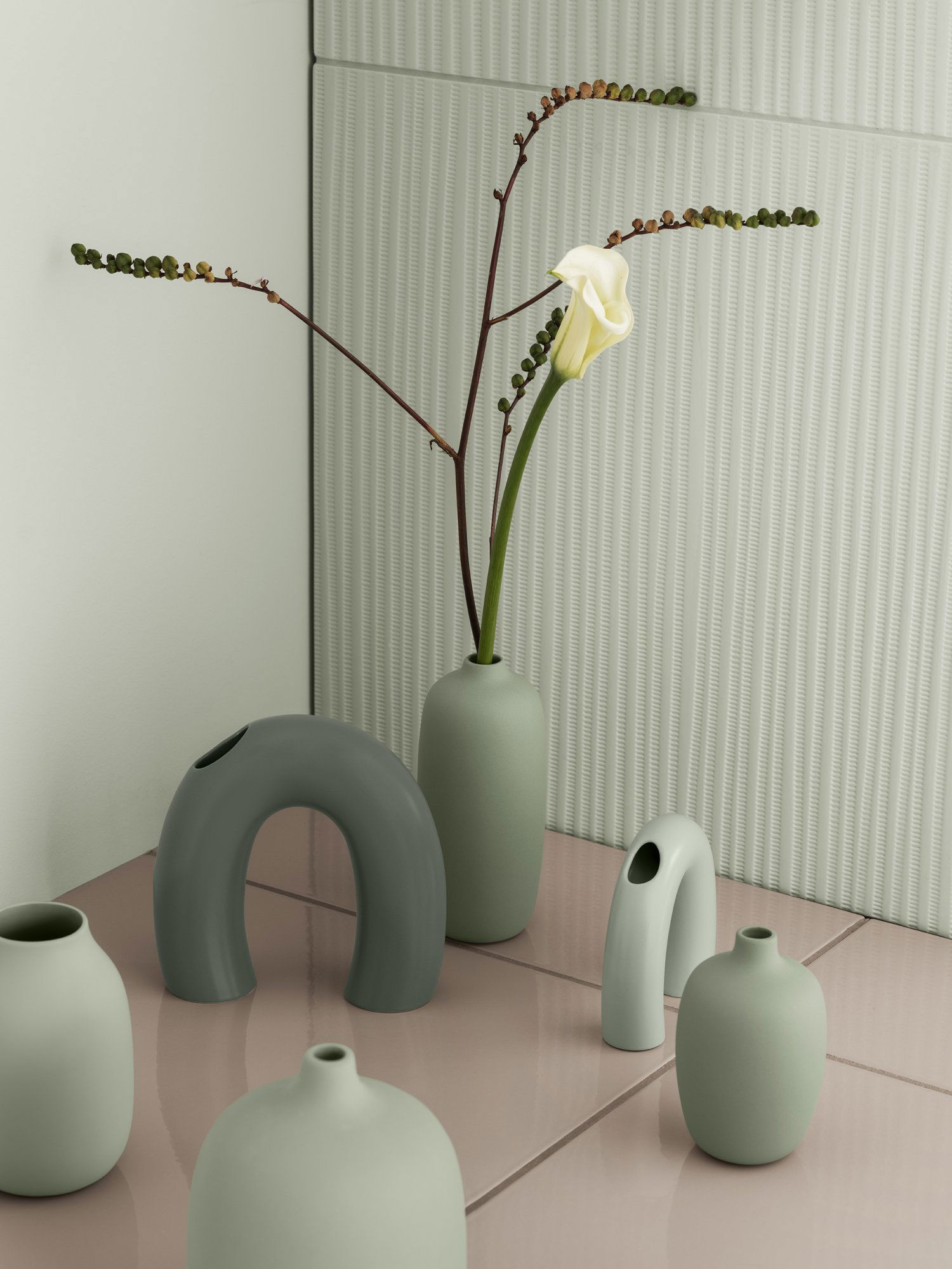 Stylish vases with a calla lily and greenery on a modern tiled surface.