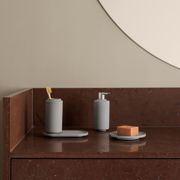 Minimalist bathroom accessories on a dark marble countertop with a round mirror.