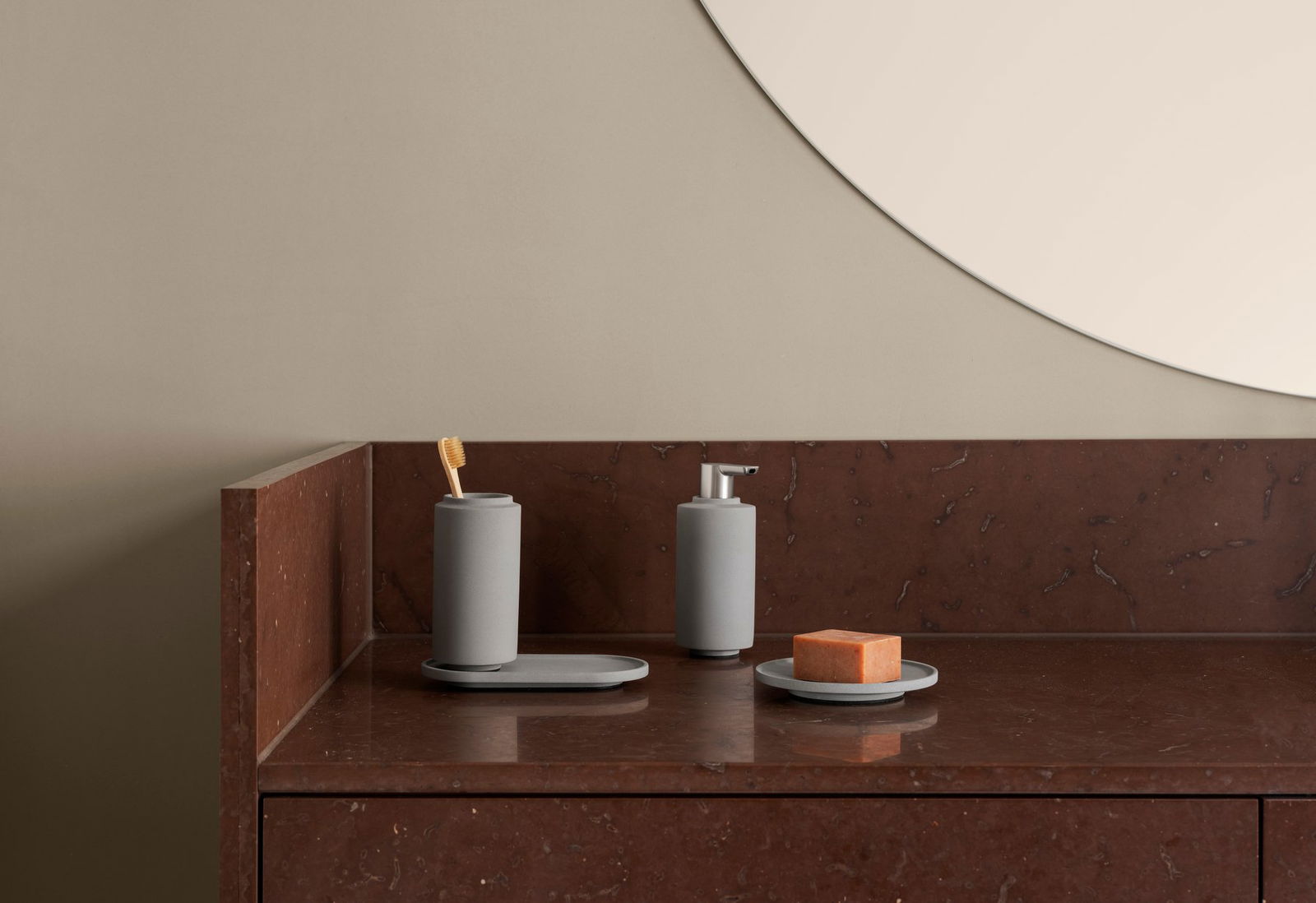 Minimalist bathroom accessories on a dark marble countertop with a round mirror.