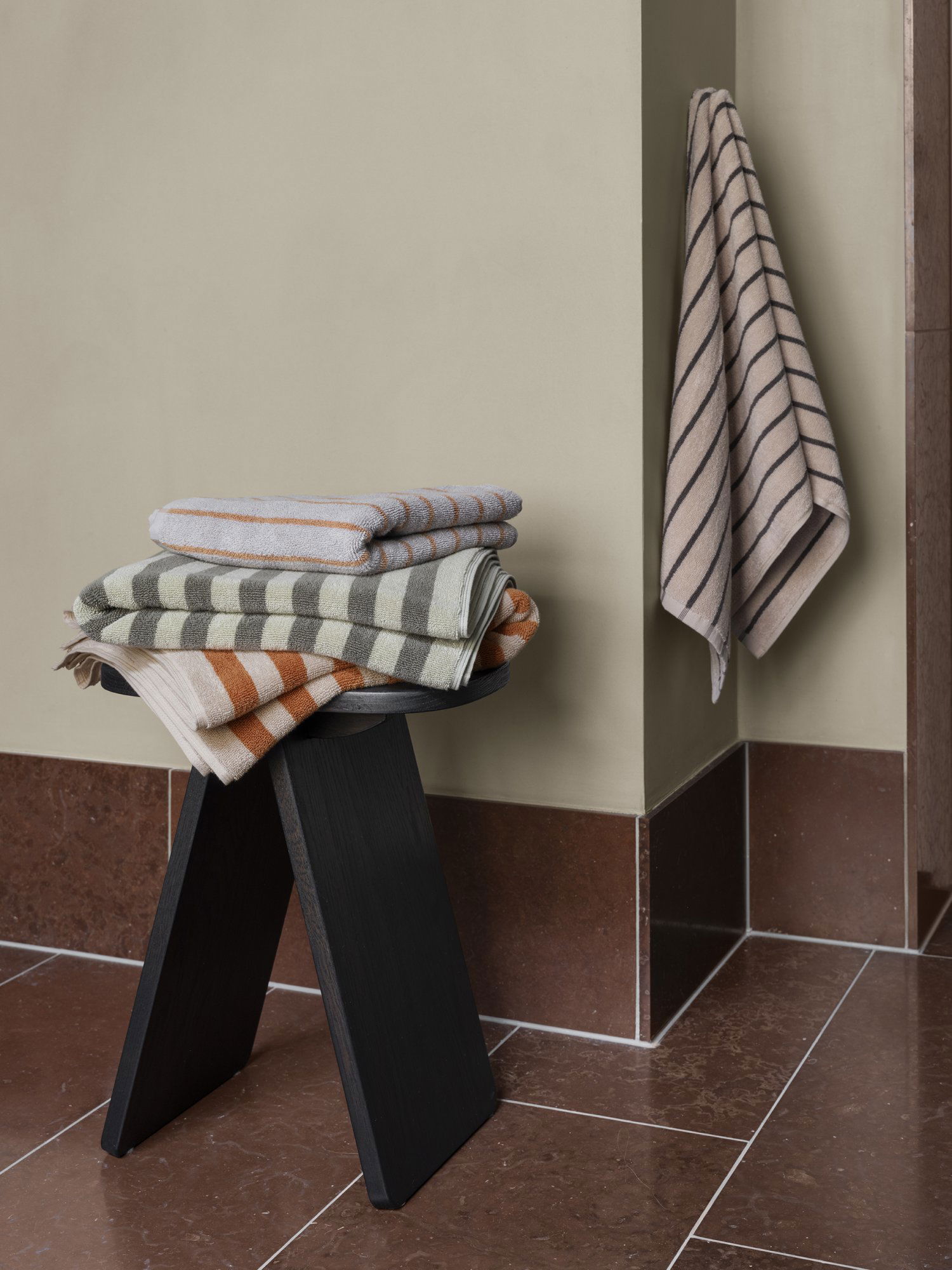 Stacked striped towels in neutral tones on a black stool against a muted wall.
