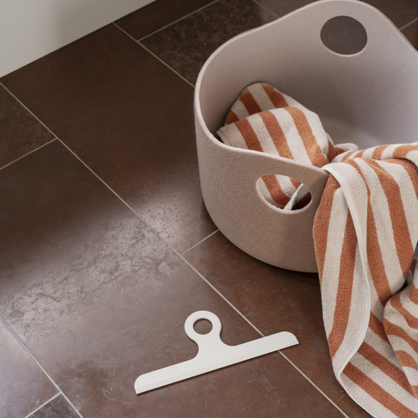 Cozy bathroom setup with a beige basket and striped towel on sleek brown tiles.
