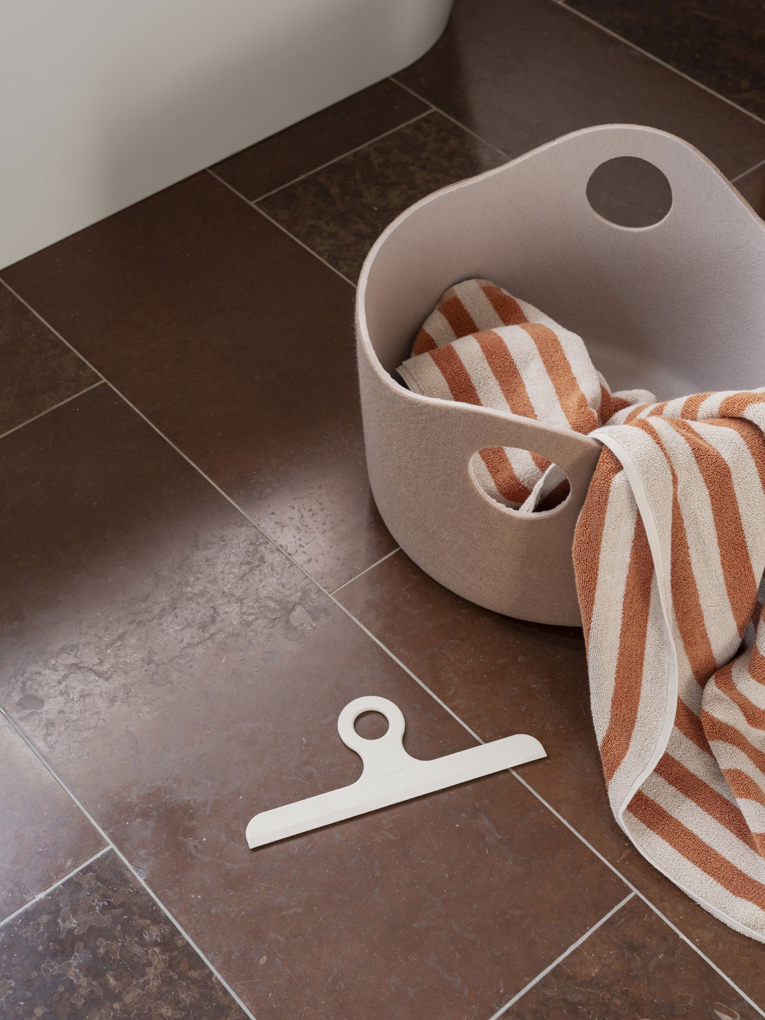 Cozy bathroom setup with a beige basket and striped towel on sleek brown tiles.