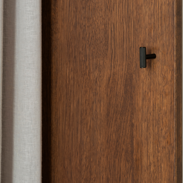 Nahaufnahme einer modernen Holztür mit einem eleganten schwarzen Türgriff und einem leichten Vorhang.
