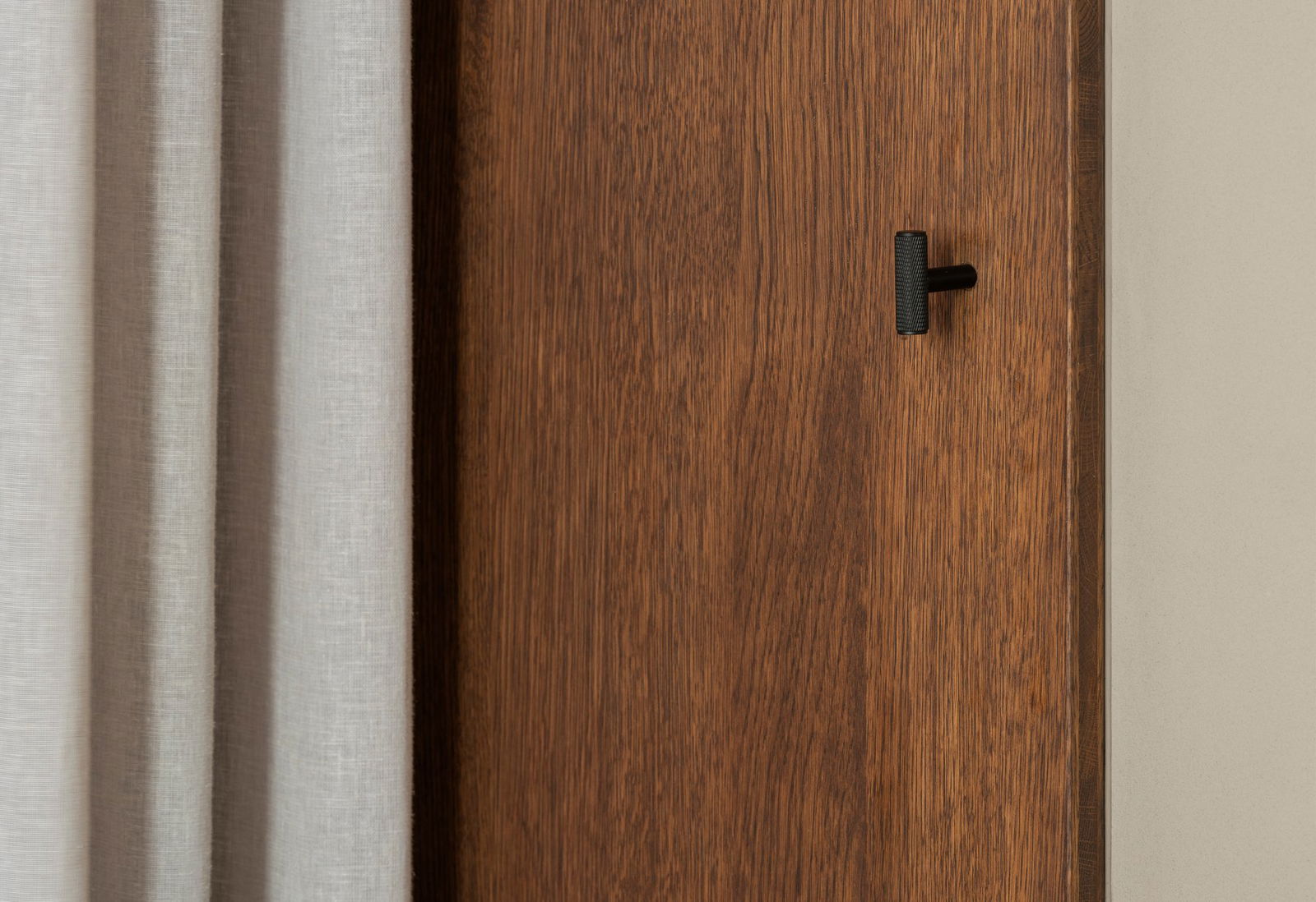 Nahaufnahme einer modernen Holztür mit einem eleganten schwarzen Türgriff und einem leichten Vorhang.