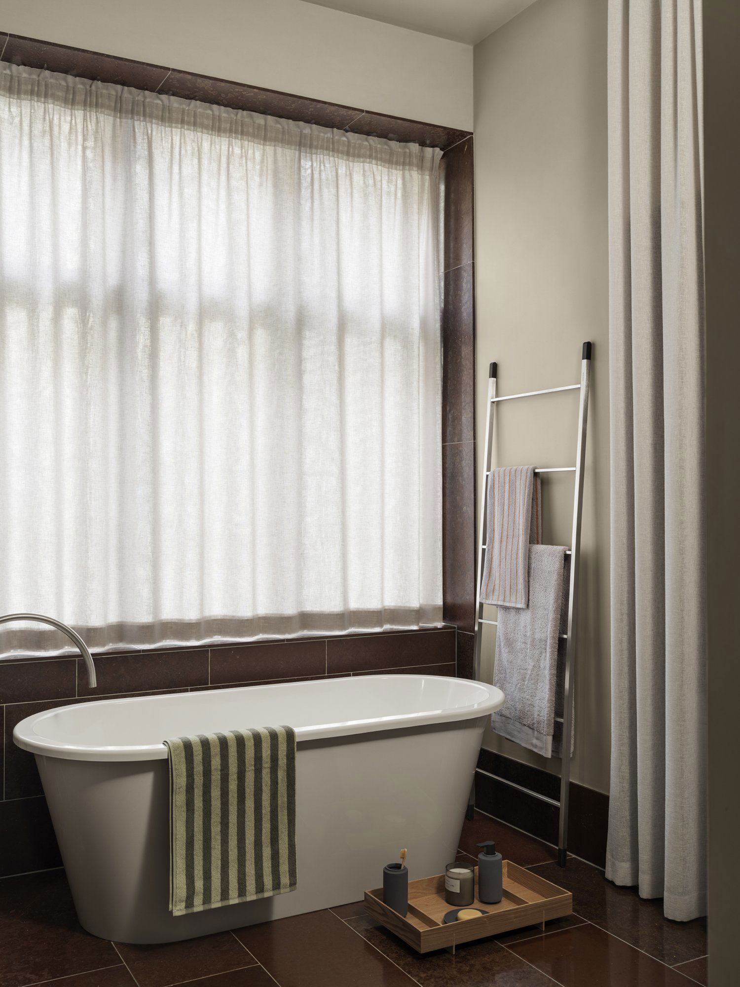 Elegant bathroom featuring a freestanding tub, natural light, and stylish textiles.