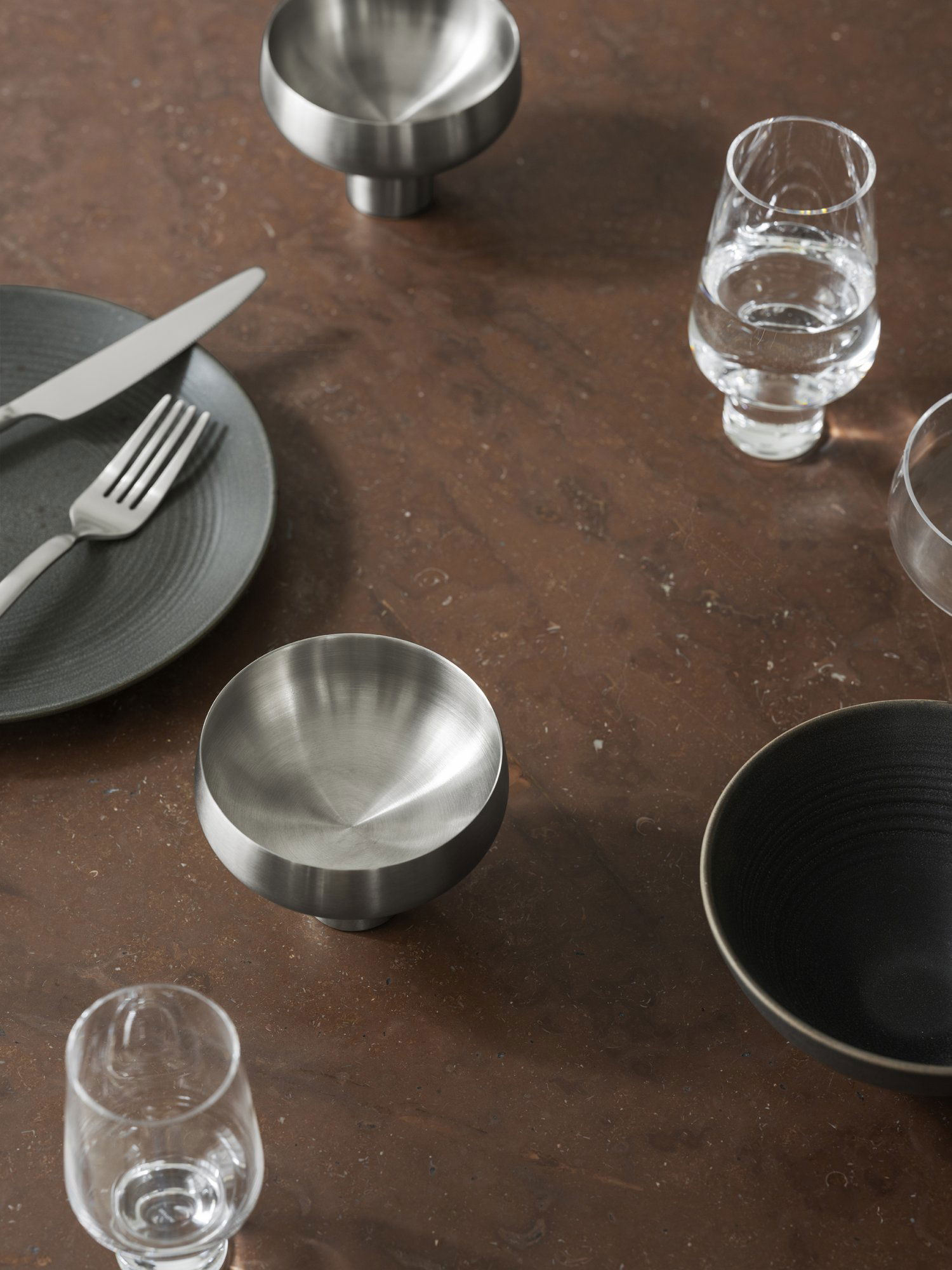 Elegant dining table set with modern stainless steel bowl and various dishware.
