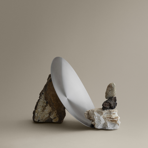 Minimalist still life featuring a metallic plate balanced on stacked rocks against a neutral backdrop.