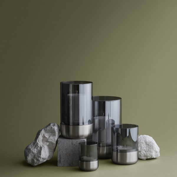 Modern candle display with smoky glass holders and natural stone accents on a green background.