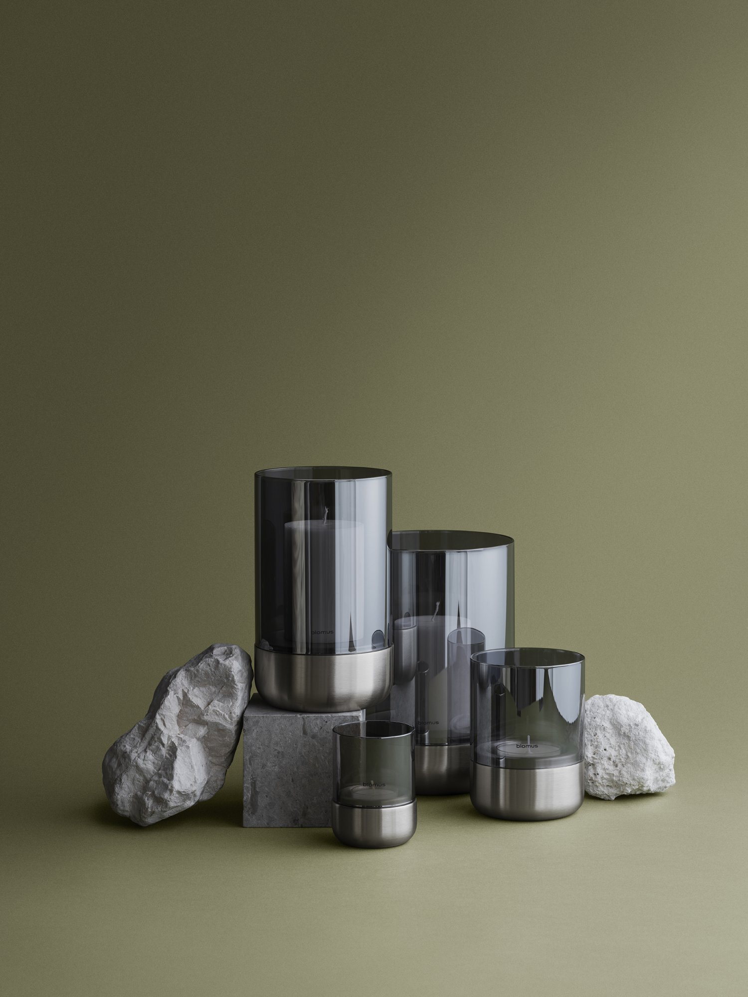 Modern candle display with smoky glass holders and natural stone accents on a green background.