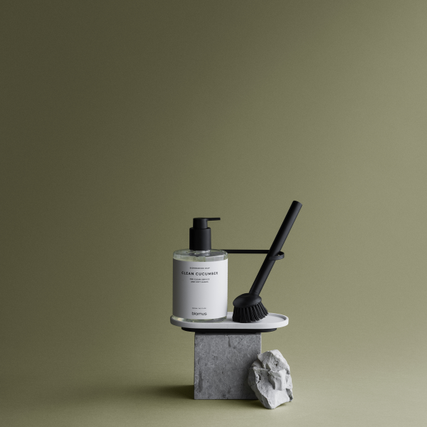 Minimalist hand soap and brush on a stone pedestal against a green background.