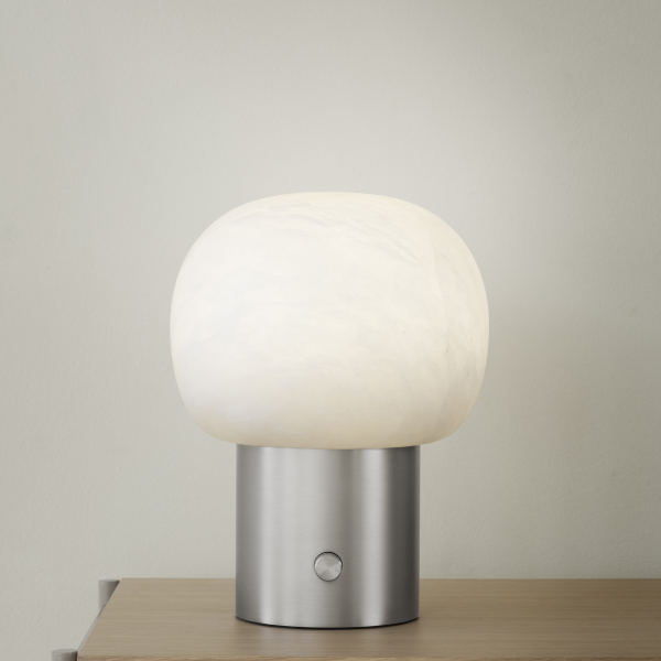 Moderne Tischlampe mit einem runden weißen Schirm und einem schlanken metallischen Fuß auf einer Holzoberfläche.