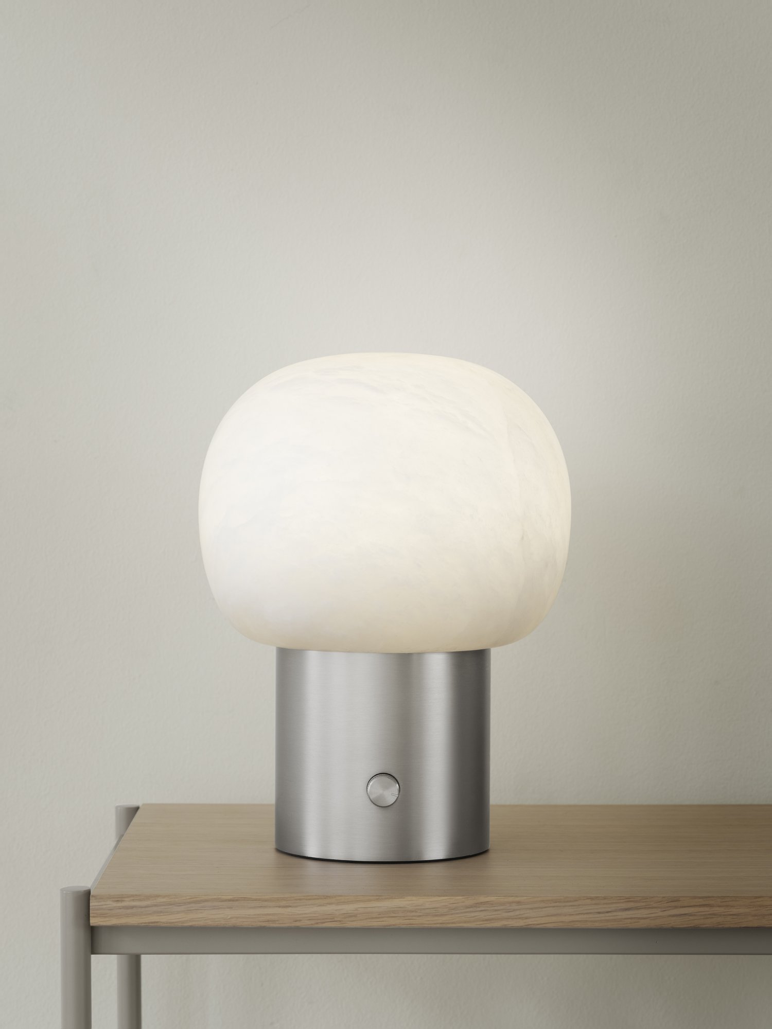 Moderne Tischlampe mit einem runden weißen Schirm und einem schlanken metallischen Fuß auf einer Holzoberfläche.