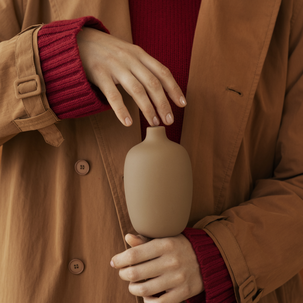 A person in a stylish coat holds a minimalist ceramic vase with hands.